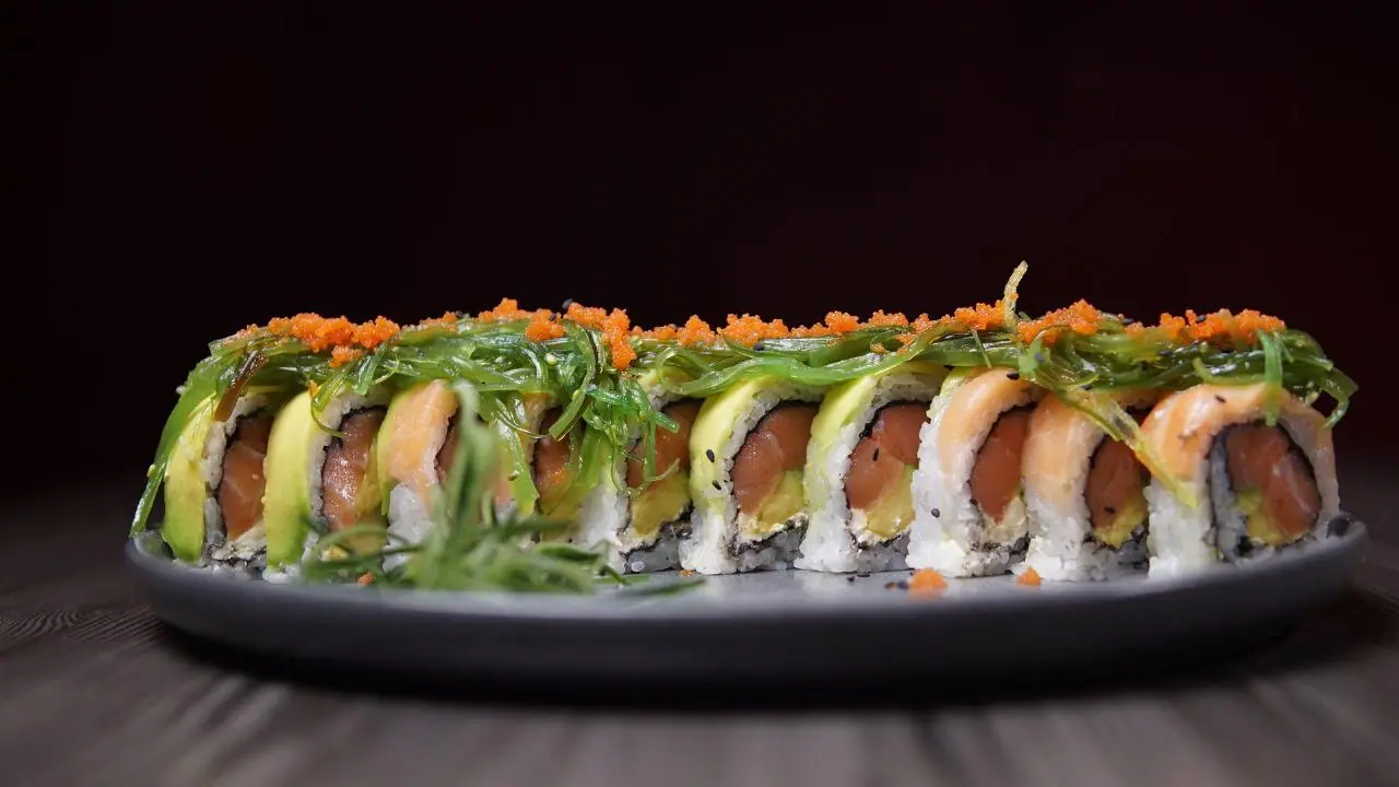 Rollo largo de sushi con salmón y aguacate sobre plato oscuro
